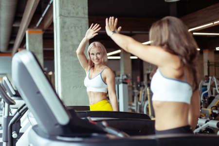 Two athletic women greet each other while exercising on a treadmill. healthy lifestyleの写真素材