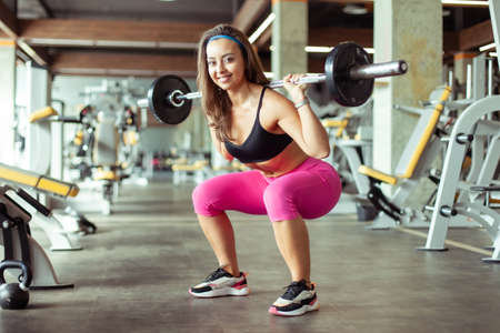Athletic beautiful woman squats with barbell on her shoulders in the gym. healthy lifestyle