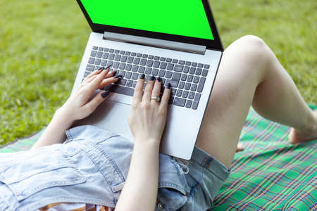 woman student uses laptop with green screen lying on a blanket in the parkの写真素材