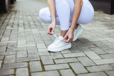 Fit woman in sports clothes ties the laces of sneakers in the cityの写真素材