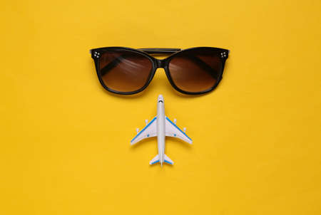 Toy passenger plane and sunglasses on yellow background. Voyage, Travel, summer vacation concept. top viewの写真素材