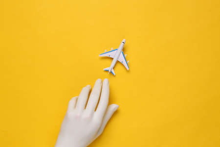 Toy passenger plane and hand on yellow background. travel concept