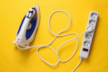 Iron for ironing and Electrical Extension cord on yellow background