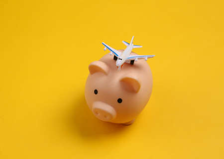 Piggy bank with toy plane on yellow backgroundの写真素材