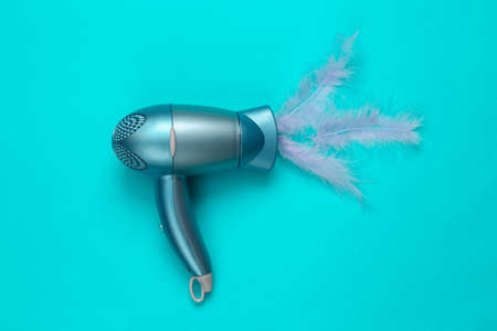 Hair dryer with feather on a blue background. minimal layout. top viewの写真素材