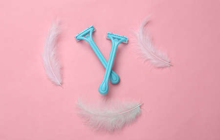 Depilatory razors and feathers on pink background. top viewの写真素材