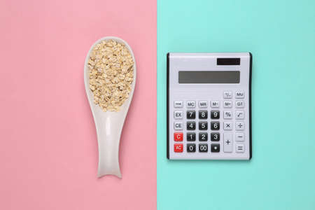 Ceramic spoon with raw oatmeal and calculator on pink blue background. top viewの写真素材
