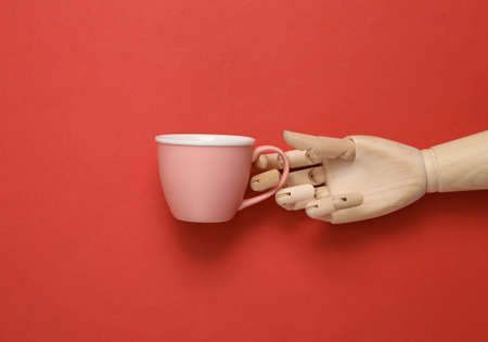 Wooden hand holding empty tea cup on red backgroundの写真素材