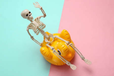 Skeleton with an inflatable duck on a yellow background. Minimal layout, Halloween party, creative layoutの写真素材