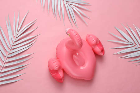 Inflatable pink flamingo with white palm leaves on pink background. top viewの写真素材
