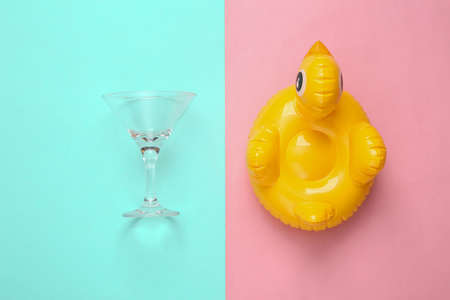 Inflatable duck and cocktail glass on pink blue background. Minimal summer party concept. top view.
