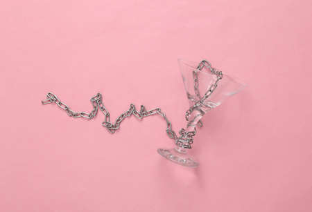 Empty cocktail glass wrapped in a chain on a pink background. Alcoholism, Prohibition of Alcohol, Stop Drinking Conceptの写真素材
