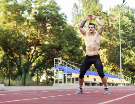 Athletic man with a naked torso practicing jumping up, warming up before running to the stadium....