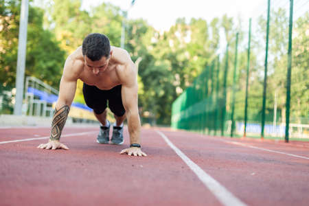 Young athletic man with a naked torso doing push-ups in the stadium.