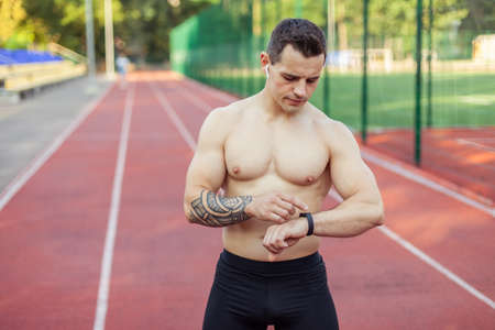 Athletic muscular man with naked torso looking at smart bracelet while monitoring heart rate at...