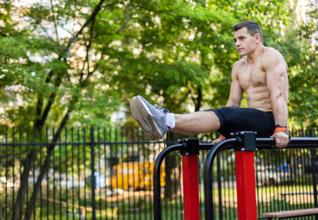 Athletic male athlete with a naked torso trains the abdominal muscles by lifting his legs up on workout ground. outdoor workoutの写真素材