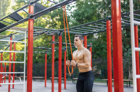 Athletic male athlete with a naked torso trains with a fitness elastic band on the workout site. outdoor workoutの写真素材