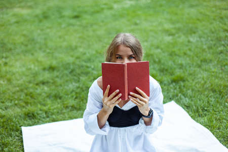 Woman covered half of her face with a book while sitting on a blanket in the parkの写真素材