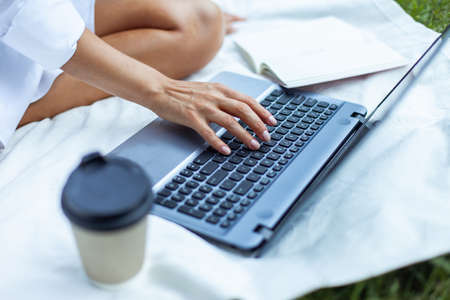 Woman using laptop while sitting on blanket in park. Freelance, remote work or educationの写真素材