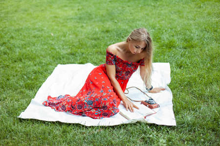 Woman in red vintage dress reading a book while sitting on a blanket in parkの写真素材