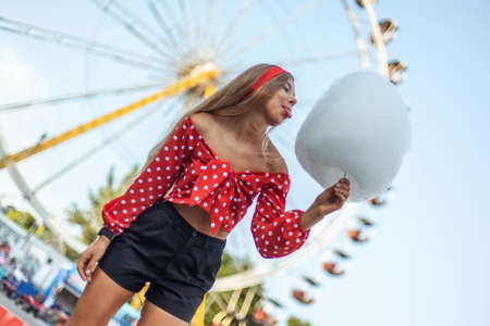 Adorable cute beautiful woman with cotton candy and penny bord stands in the middle of amusement...