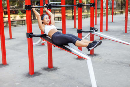 Pretty athletic woman exercising abdominal muscles on modern sports ground