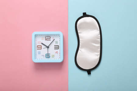 Sleep mask and alarm clock on a blue-pink background. Insomnia concept. top view