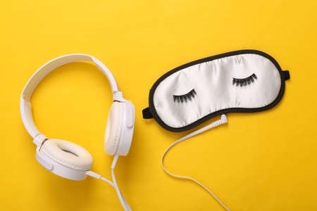 Relaxing sleep music. Sleep mask with eyelashes and headphones on yellow background
