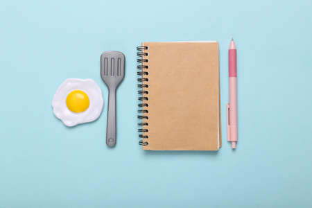 cooking recipes. Notepad with plastic scrambled eggs and a spatula for cooking on a blue background