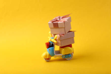 Toy scooter with a gift box on yellow background. Delivery concept, Christmas compositionの写真素材