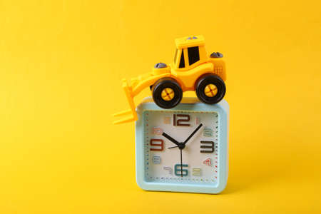 Toy forklift with alarm clock on yellow background