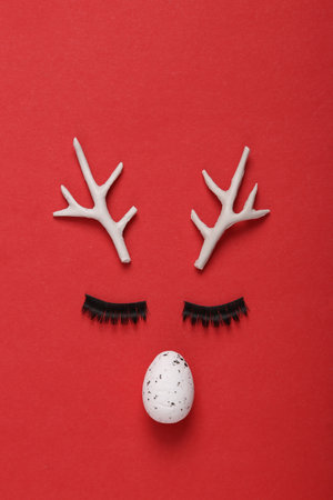 Deer face with horns, eyelashes and an egg on a red background. Symbolism, allegoryの写真素材