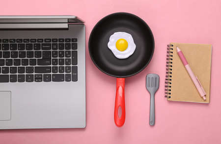 Culinary blog. Laptop, toy frying pan with scrambled eggs and notepad on pink background