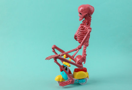 Humorous shot of a pink skeleton riding a small scooter. blue backgroundの写真素材