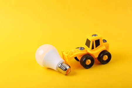 Toy forklift with light bulb on yellow background