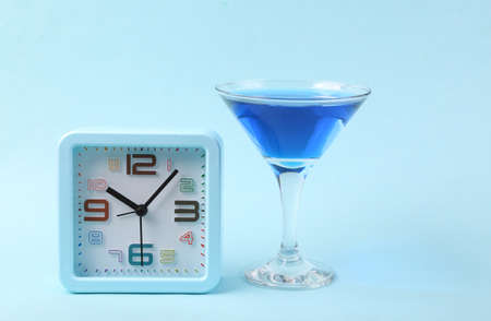 Margarita blue cocktail with alarm clock on blue background. party concept