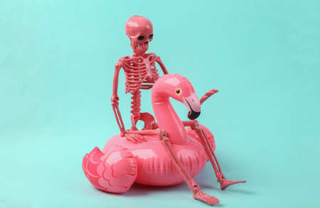 Skeleton with pink inflatable flamingo on blue background. halloween party conceptの写真素材