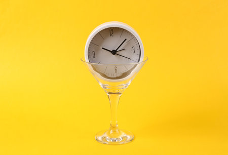 Alarm clock in cocktail glass on yellow background. fresh ideas. Minimal party concept, creative...