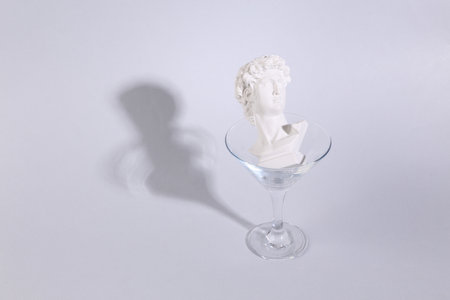 Plaster bust of David in cocktail glass on gray background. fresh ideas. Minimal party concept, creative layoutの写真素材