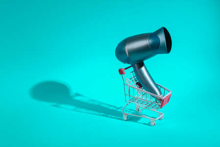 White shopping trolley with hair dryer on turquoise background, long shadow. minimal love layout