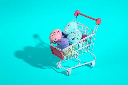 Mini shopping cart with colored easter eggs on turquoise backgroundの写真素材