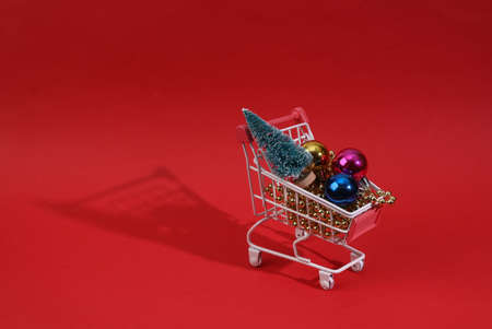 Mini shopping cart with christmas toys, Christmas tree and garlands on red backgroundの写真素材