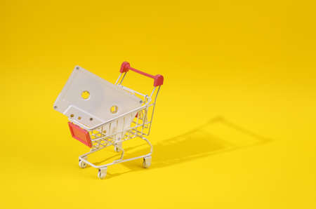 Mini shopping cart with audio cassette on yellow bright background