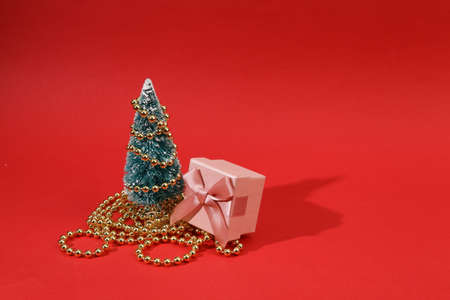 Mini Christmas tree with garland and gift box on red background