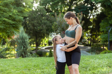 Maternal love and care. Little daughter hugs her fit mom in the park. Healthy lifestyle, fitnessの写真素材