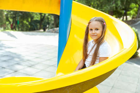 Little girl is sliding down the slide in the playgroundの写真素材