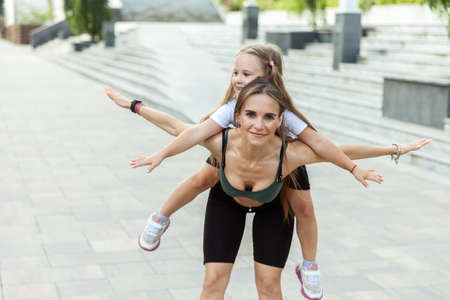 Active fit mom with daughter on her back having fun, piggy back outdoorsの写真素材