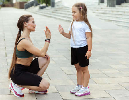 Fit mom with little daughter high five outdoors. team training. An active family. mom trainerの写真素材