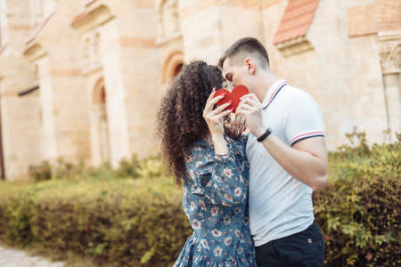 Beautiful young couple holding a heart, kissing, showing their love against the background of urban architecture. love, romantic conceptの写真素材