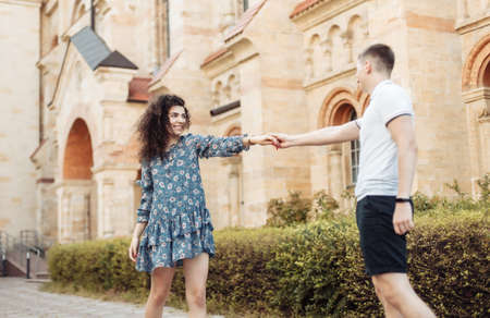 follow me. Young woman pulls a young guy along while walking against the background of old european architectureの写真素材